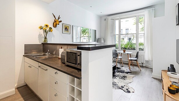 Una cocina moderna con una isla central, una zona de comedor con una mesa y sillas, y un amplio ventanal que proporciona luz natural.