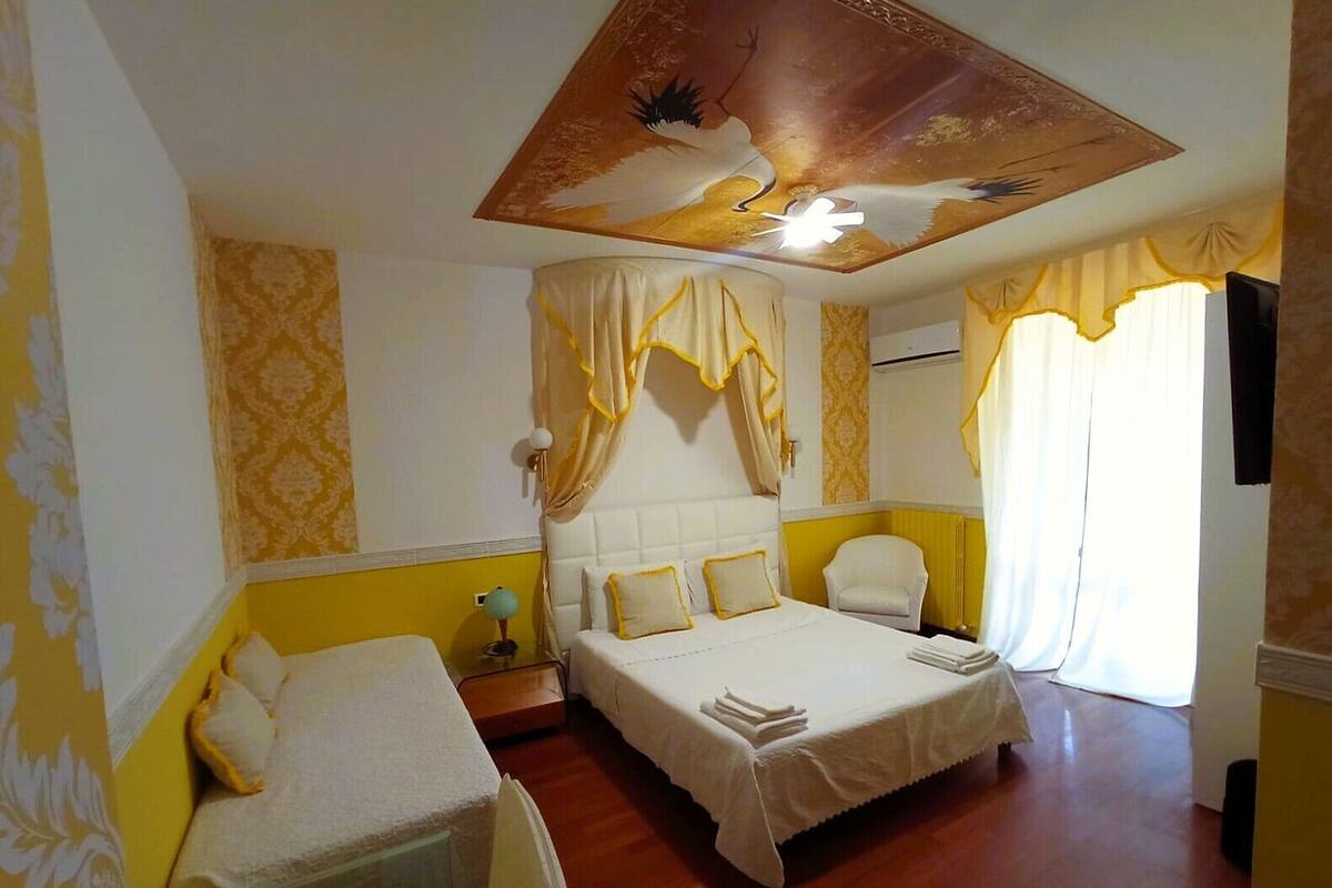 Une chambre d’hôtel avec deux lits, un ventilateur de plafond, une chaise et une grande fenêtre avec des rideaux.