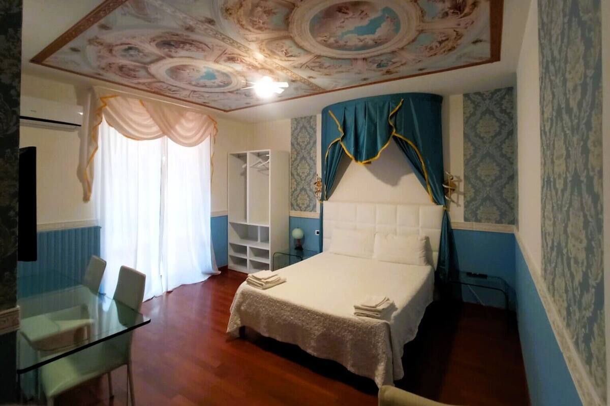 Une chambre à coucher comprenant un lit, une table en verre, des chaises, une armoire et un plafond orné d’un motif décoratif.