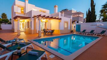Una villa moderna con piscina, mobiliario de exterior y una pérgola.