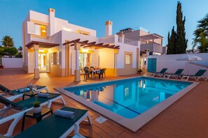 Una villa moderna con piscina, mobiliario de exterior y una pérgola.