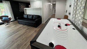Ett modernt vardagsrum med ett biljardbord, en svart lädersoffa och en vägg med ett mönster.