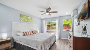A bedroom with a bed, a ceiling fan, a nightstand, a window with curtains, and a view of greenery outside. - NEW! FULLY UPDATED ground floor condo with AC! (Kapaʻa)
