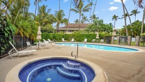 A pool area with lounge chairs and umbrellas, surrounded by palm trees and a building in the background. - NEW! FULLY UPDATED ground floor condo with AC! (Kapaʻa)