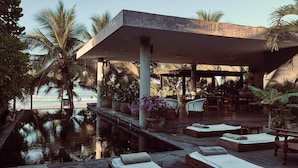 Un espace aménagé au bord de la piscine, avec des chaises longues, un coin salon abrité et des palmiers.