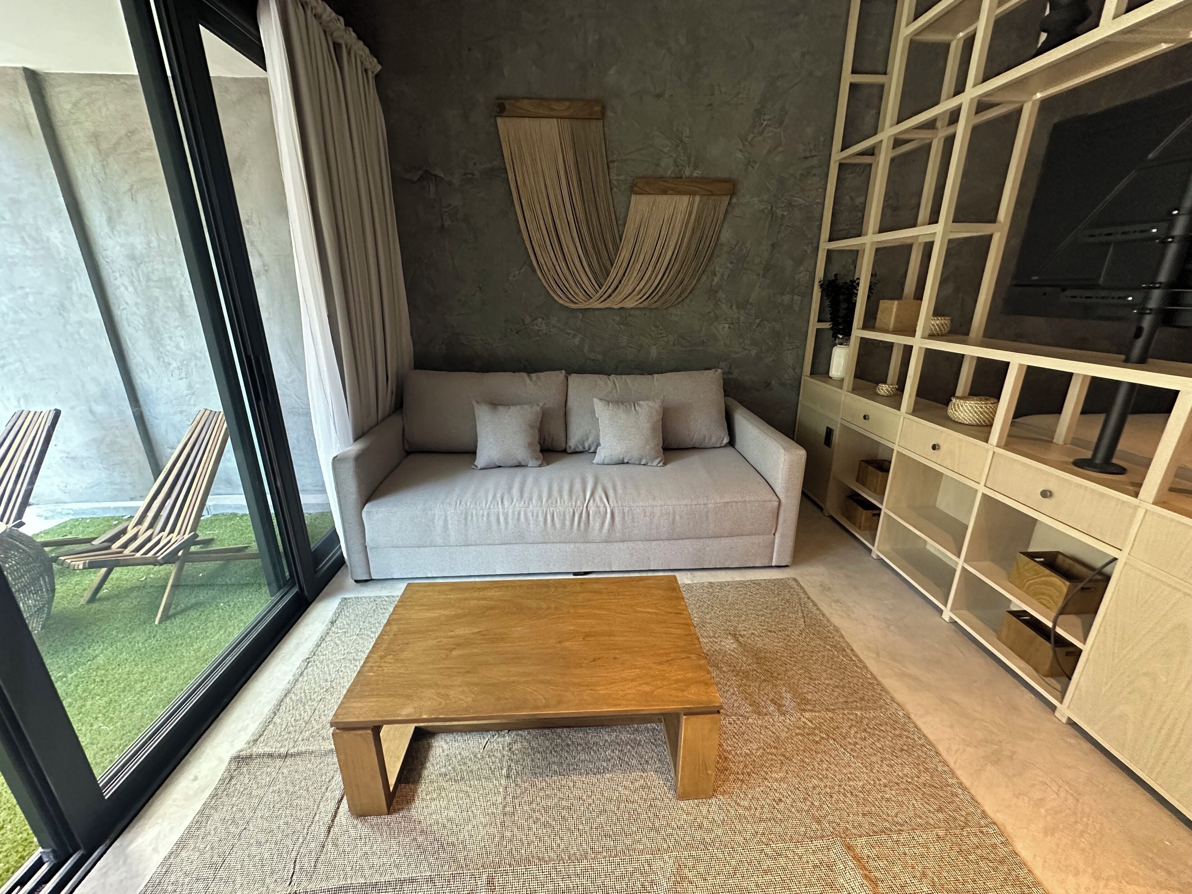 A modern living room with a light grey sofa, a wooden coffee table, and a large window with curtains.