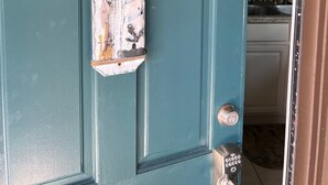 Une porte de couleur bleu-vert, ornée d’une enseigne patinée sur laquelle on peut lire « BIENVENUE, AMIS », et d’un élément décoratif placé au-dessus.