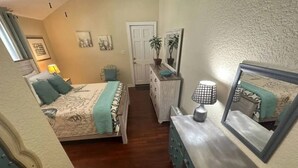 Een slaapkamer met een bed, een kaptafel, een spiegel en een deur naar een andere kamer.