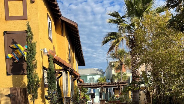 A courtyard with potted plants, outdoor furniture, and a building with a yellow facade. - Unit Number 4 (New Smyrna Beach)