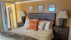 A neatly made bed with a patterned bedspread, two bedside lamps, and a nightstand with a drawer. - Unit Number 4 (New Smyrna Beach)