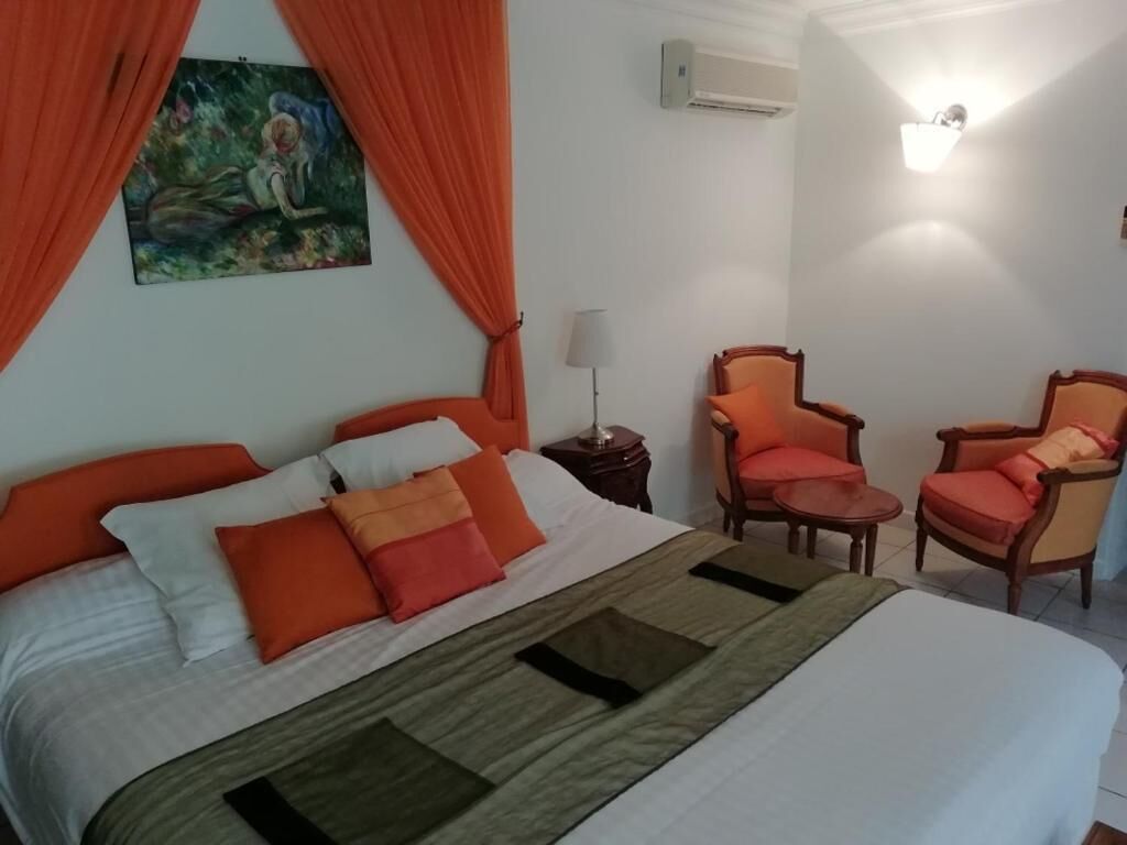 A hotel room with a bed, two armchairs, a nightstand, and a painting on the wall.