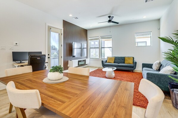 A modern living room with a wooden dining table, white chairs, a grey sofa, and a red rug.