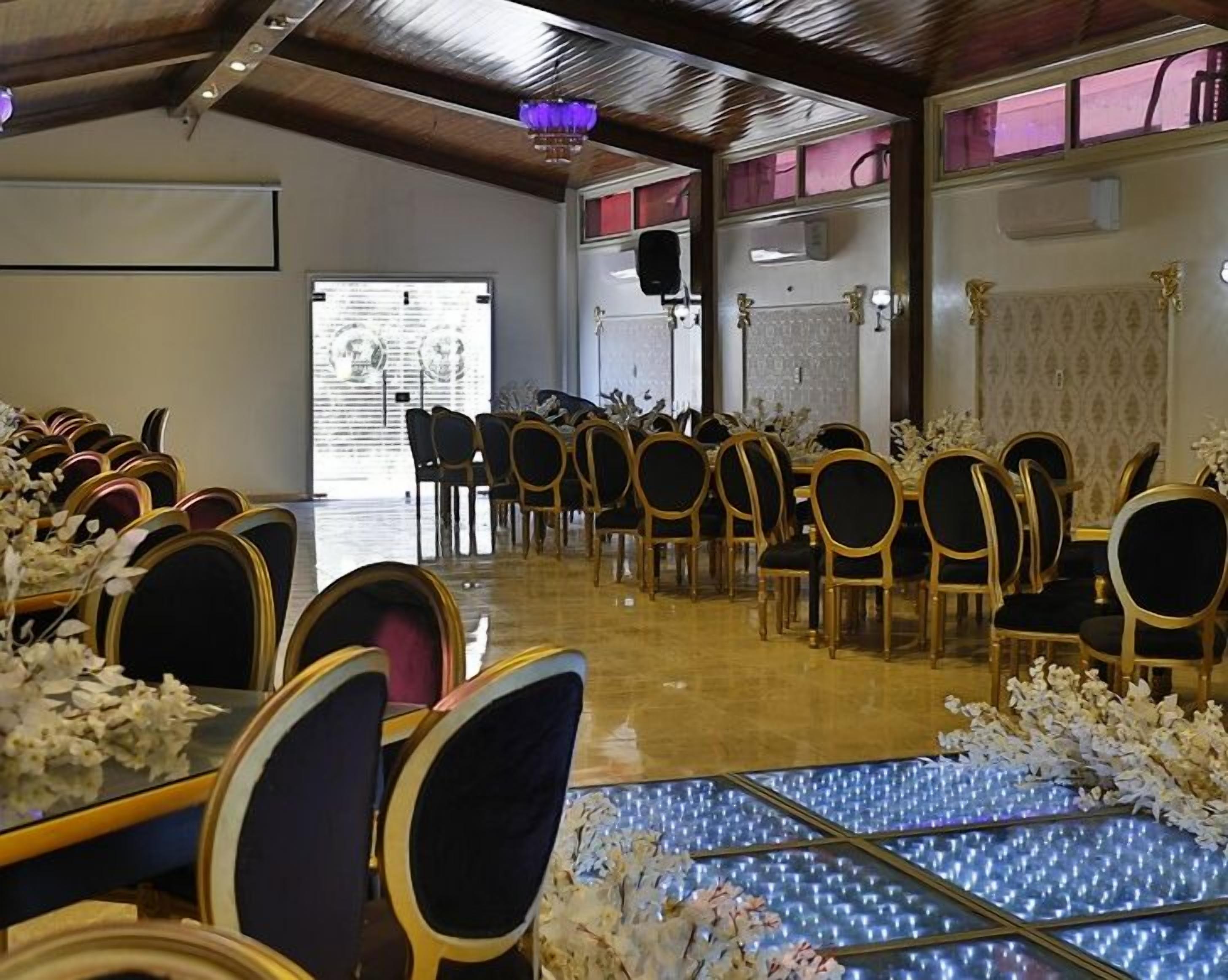 A banquet hall with rows of tables and chairs, a stage with a podium, and a large window.