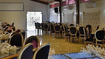 A banquet hall with rows of tables and chairs, a stage with a podium, and a large window.