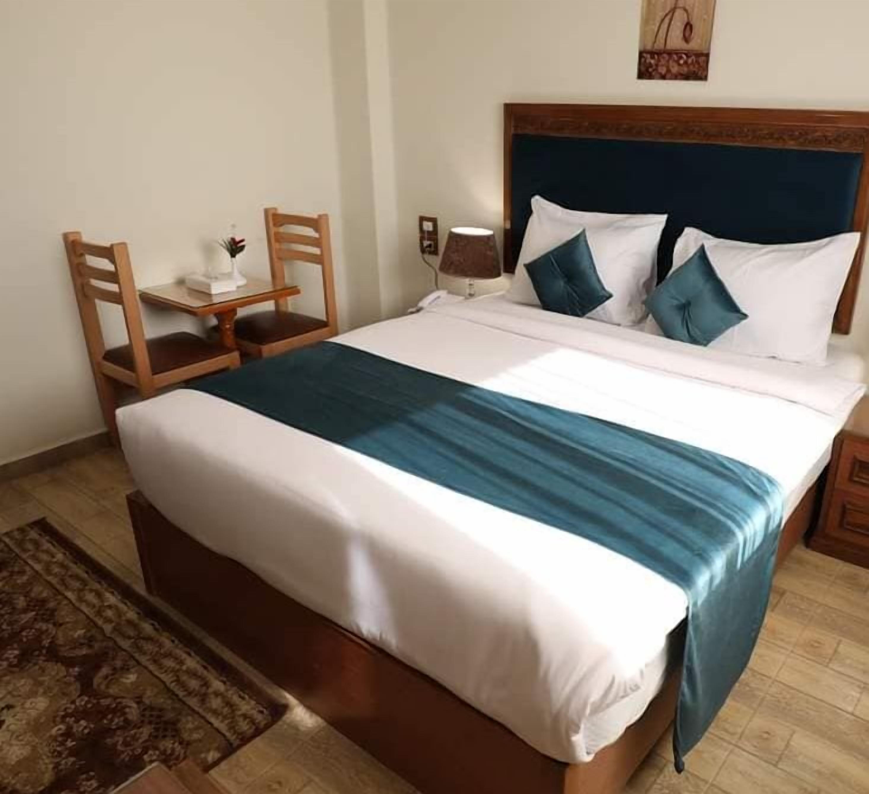 A hotel room with a bed, a nightstand, a lamp, a chair, and a small table.