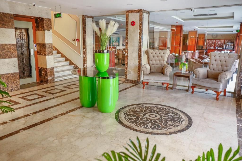 Un vestíbulo con una escalera de mármol, un jarrón verde con plantas y una zona de estar con sillones acolchados.