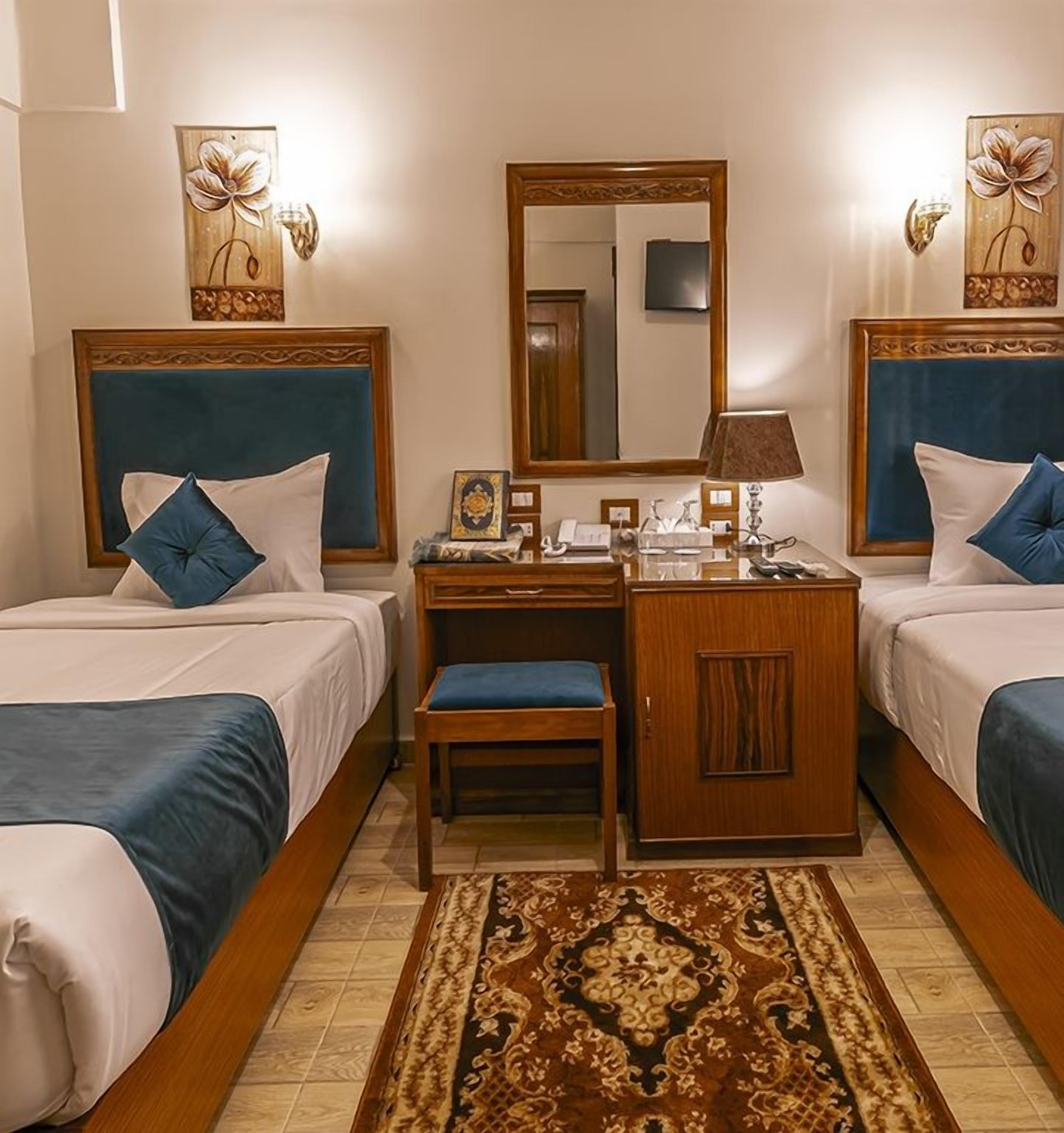 A hotel room with two beds, a desk, a chair, a mirror, and a decorative rug.