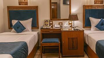 A hotel room with two beds, a desk, a chair, a mirror, and a decorative rug.