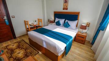 A hotel room with a bed, bedside tables, a chair, a rug, and a painting on the wall.