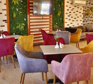 Un intérieur moderne avec un espace salon comprenant un mélange de canapés et de fauteuils, un téléviseur à écran plat fixé au mur et un mur végétal décoratif.