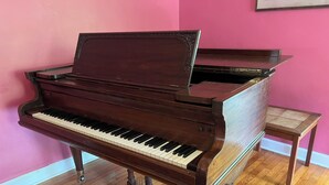 A grand piano in a room with wooden flooring and pink walls.