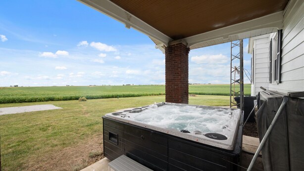 Ein Whirlpool auf einer Veranda mit Blick auf ein Wiesenfeld und einen klaren Himmel.