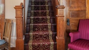 Eine Holztreppe mit einem gemusterten Teppich, eine Holztür und ein rot gepolsterter Sessel.
