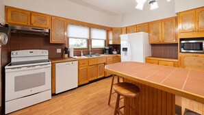 Eine Küche mit Holzschränken, einem weißen Herd, einer Spülmaschine, einem Kühlschrank und einem Barhocker.