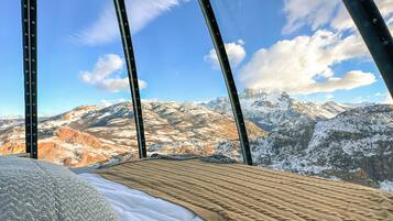 A bed with a view of snow-covered mountains and a clear sky.