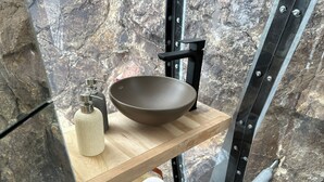 A bathroom with a stone wall, a wooden shelf with a bowl sink, a soap dispenser, and toilet paper. - OVO Patagonia (El Chalten)