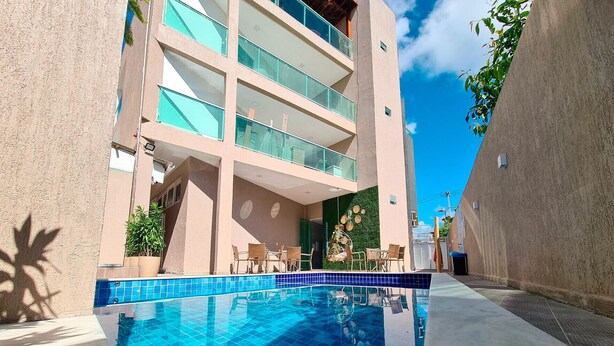 Un edificio moderno con piscina, mobiliario exterior y un cielo azul despejado.