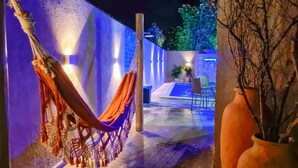 Una hamaca colgada en una pared, con una piscina y sillas al fondo.