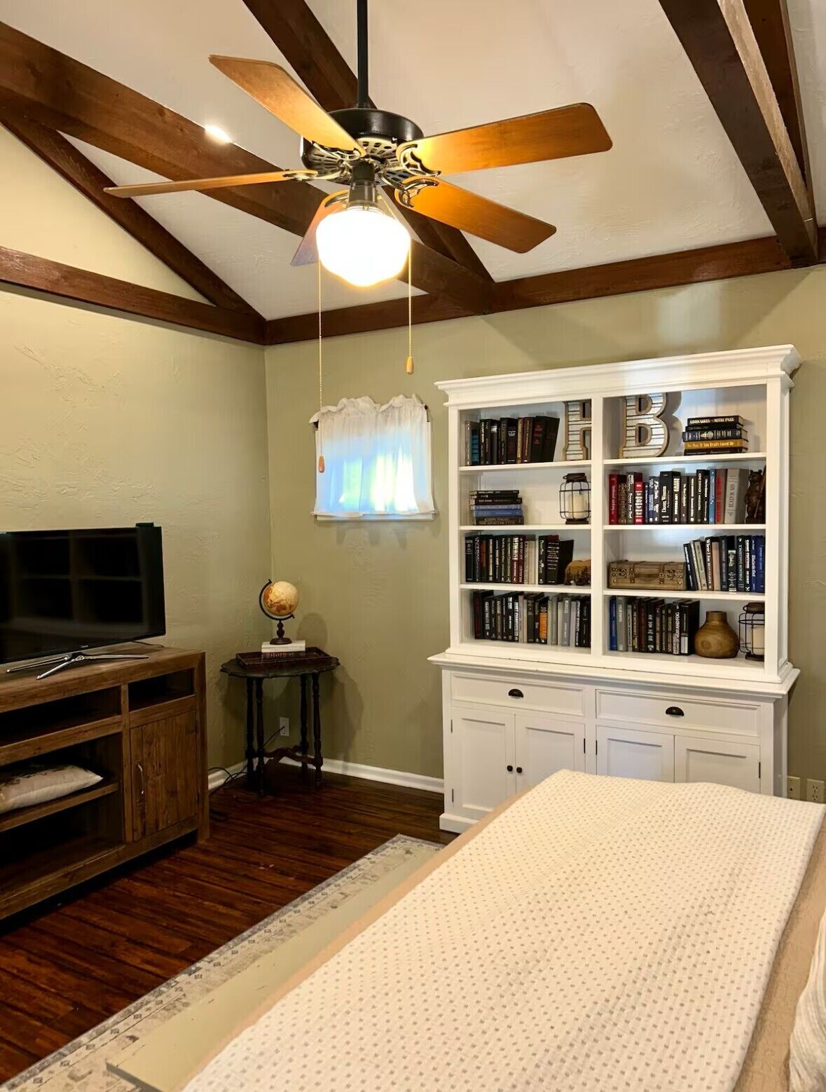 Ein Schlafzimmer mit Bett, Bücherregal, Fernseher und Deckenventilator.