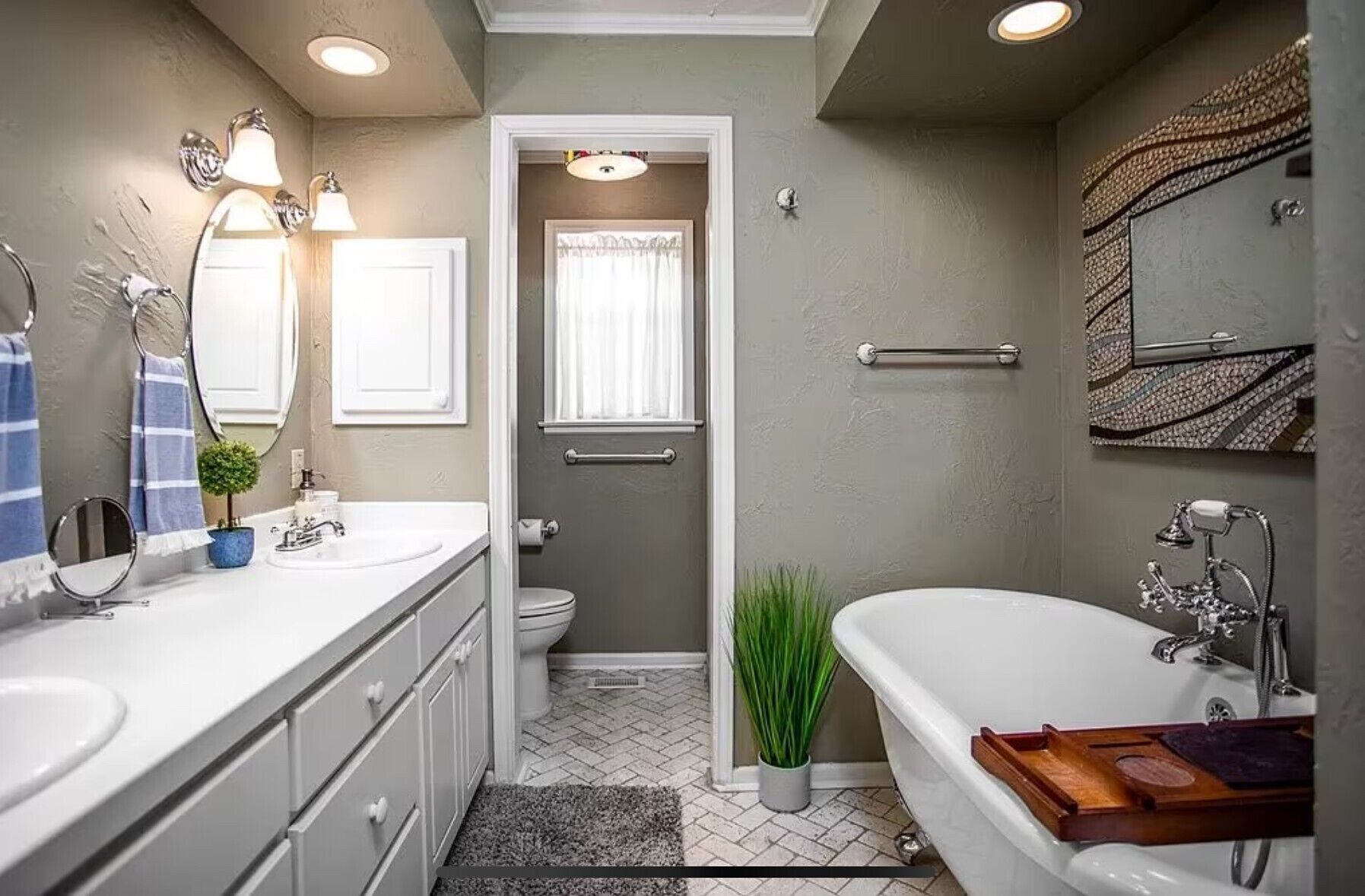 Een badkamer met een witte badkuip, een wastafel met spiegel en een toilet. Er staat een klein plantje en er is een handdoekhouder.
