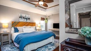 Un dormitorio con cama, ventilador de techo, televisor y espejo.