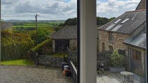 Une vue depuis une fenêtre donnant sur un paysage rural, avec des bâtiments en pierre, une cour en gravier et une clôture en bois.