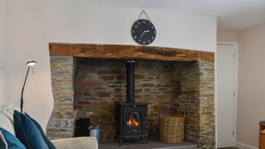 Un salon avec une cheminée en pierre, une horloge, un canapé avec des coussins et un lampadaire.