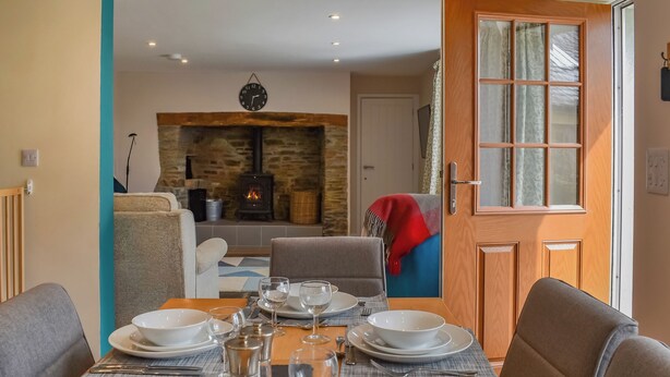 Un coin repas avec une table dressée pour quatre personnes, une cheminée en pierre et une vue sur le salon.
