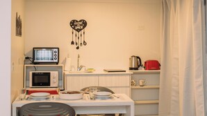 Eine kleine Küche mit Mikrowelle, Toaster und Wasserkocher auf der Arbeitsplatte, einem Esstisch mit Stühlen und einer weißen Wand mit einer Küchendekoration.
