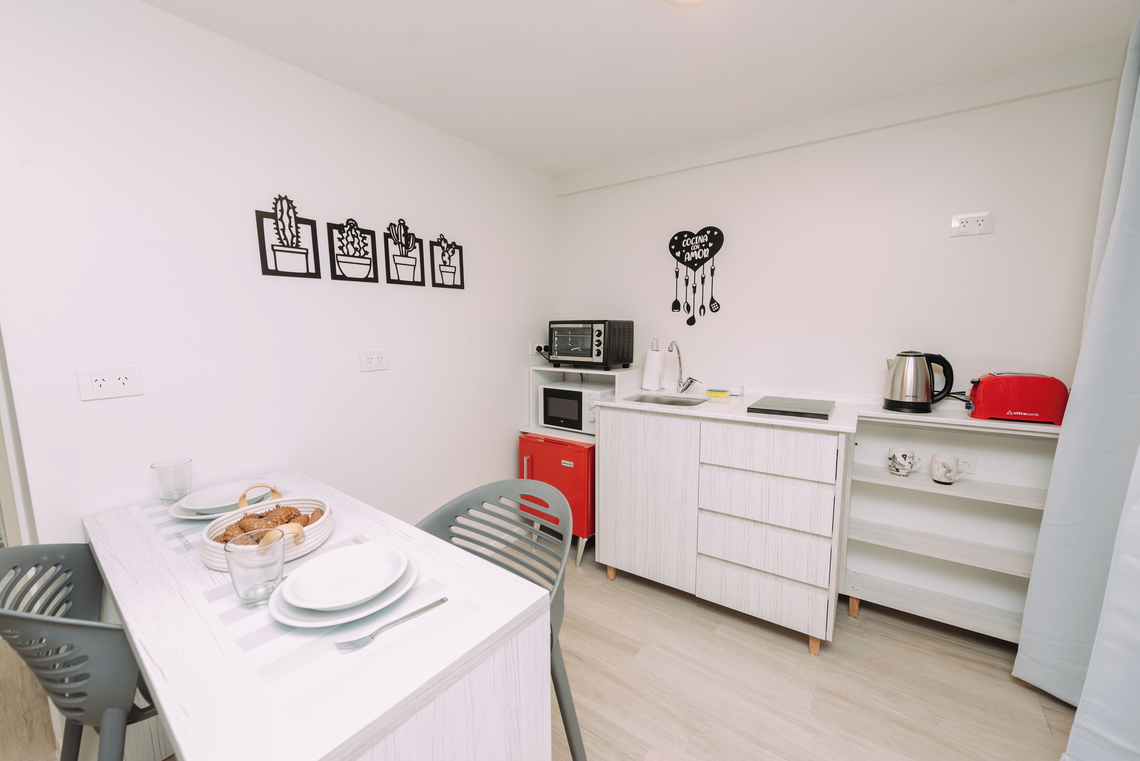 A compact kitchen with white cabinets, a microwave, a kettle, and a red appliance on the countertop.