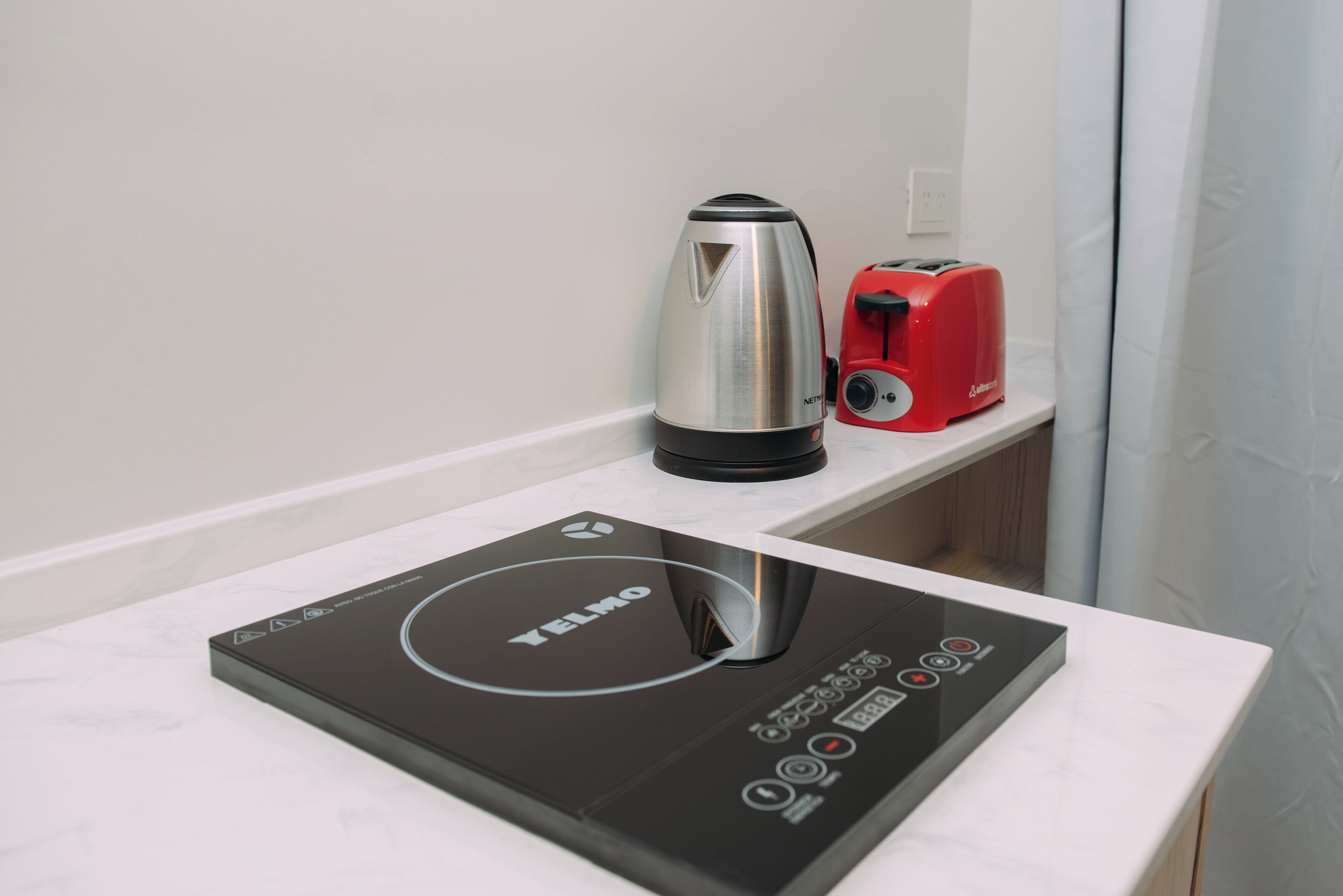 A kitchen counter with a black induction cooktop, a silver kettle, and a red toaster.
