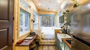 Ein gemütliches Blockhaus mit Holzinnenraum, einem Bett, einer kleinen Küche und einem Schachbrett auf einem Schreibtisch.