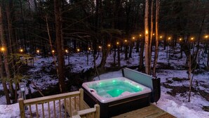Ein Whirlpool in einem verschneiten Wald mit einer Holterrasse und Lichterketten.