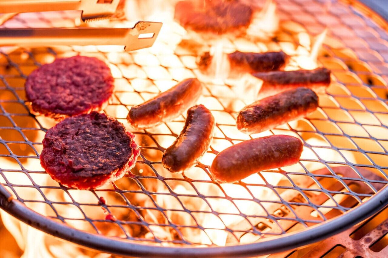 Una parrilla con hamburguesas y salchichas asándose sobre fuego abierto.