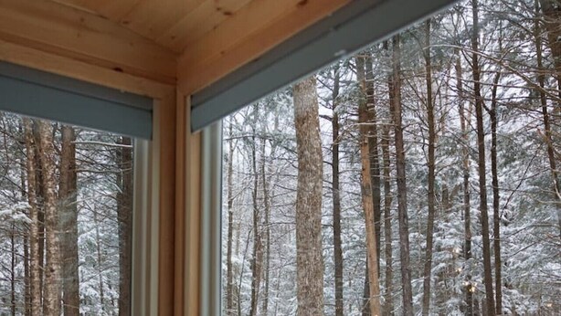 Una cabaña con un amplio ventanal que ofrece vistas a un bosque nevado.
