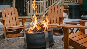 Una chimenea con sillas alrededor, una terraza de madera y un edificio al fondo.