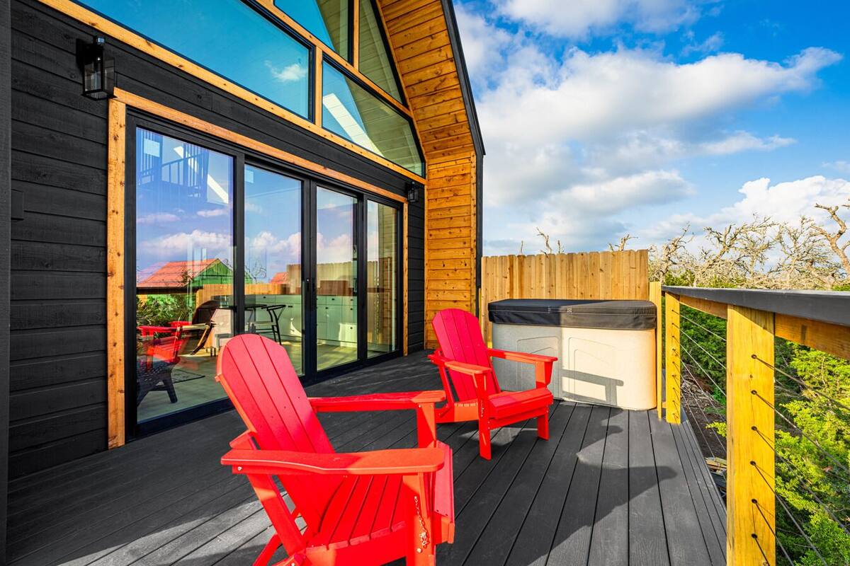 A wooden deck with two red Adirondack chairs, a hot tub, and a glass-enclosed patio area.