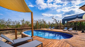 A wooden deck with a swimming pool, lounge chairs, and a covered area with a table and chairs. - Astryia Glamping (Fredericksburg)