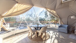 A tented room with a round table and chairs, a sofa, and a view of the outdoors. - Astryia Glamping (Fredericksburg)