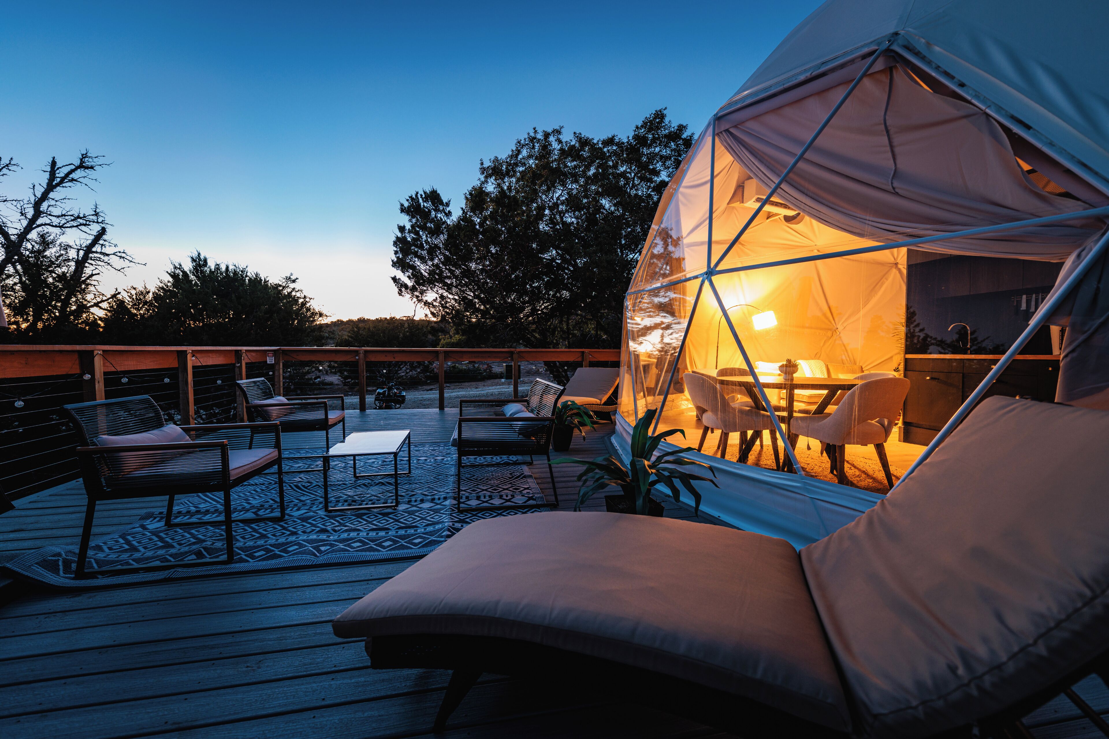 A cozy outdoor seating area with a transparent dome structure, wooden deck, and lounge chairs.